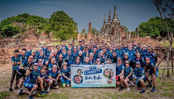 A group photo of cyclists holding a banner for the 2019 Charity Bike Ride in front of ancient ruins in Thailand