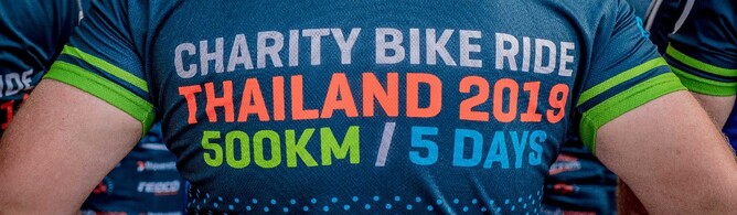 Close-up of a person's back wearing a blue and green jersey with the text "Charity Bike Ride Thailand 2019 500KM / 5 DAYS" printed on it