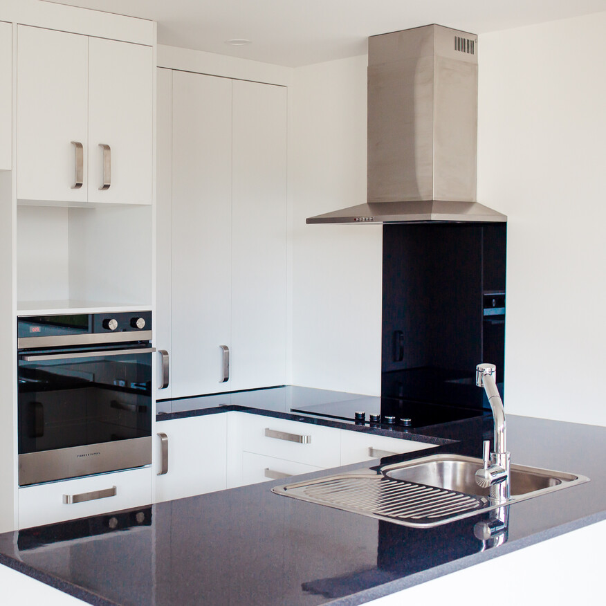 Modern kitchen with white cabinets, black countertops, a built-in oven, a stainless steel range hood, and a sleek sink