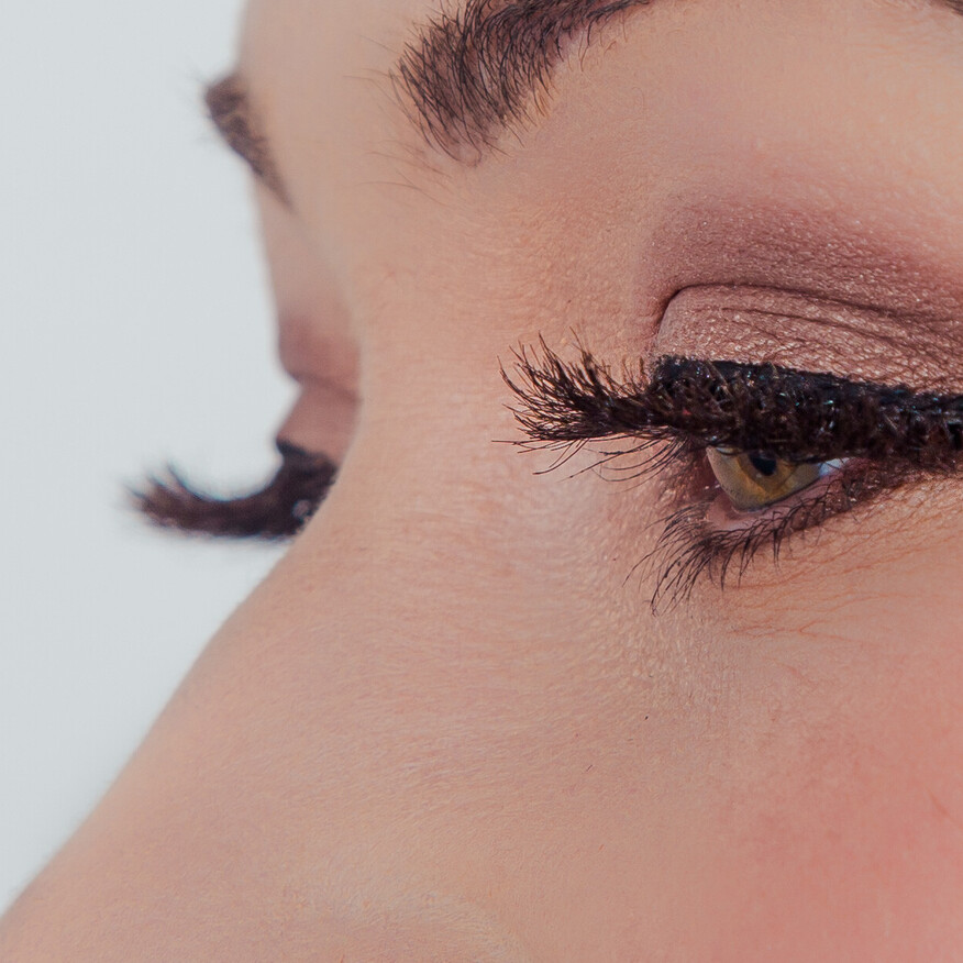 Close-up of an eye with winged eyeliner, shimmery eyeshadow, and long, voluminous false lashes