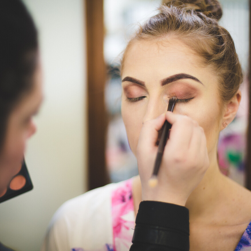 A makeup artist applies eyeshadow to a woman's eyelid, with a blurred background