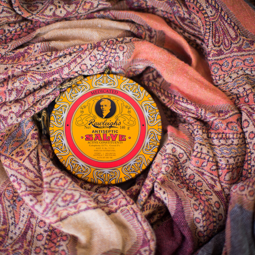A tin of Rawleigh’s Antiseptic Salve with a yellow and red vintage-style label sits nestled in a richly patterned fabric
