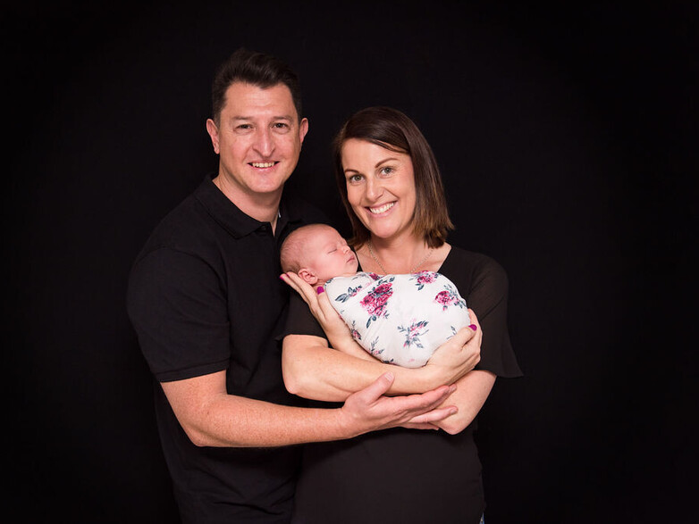 Mum and Dad holding newborn baby girl on a black backdrop