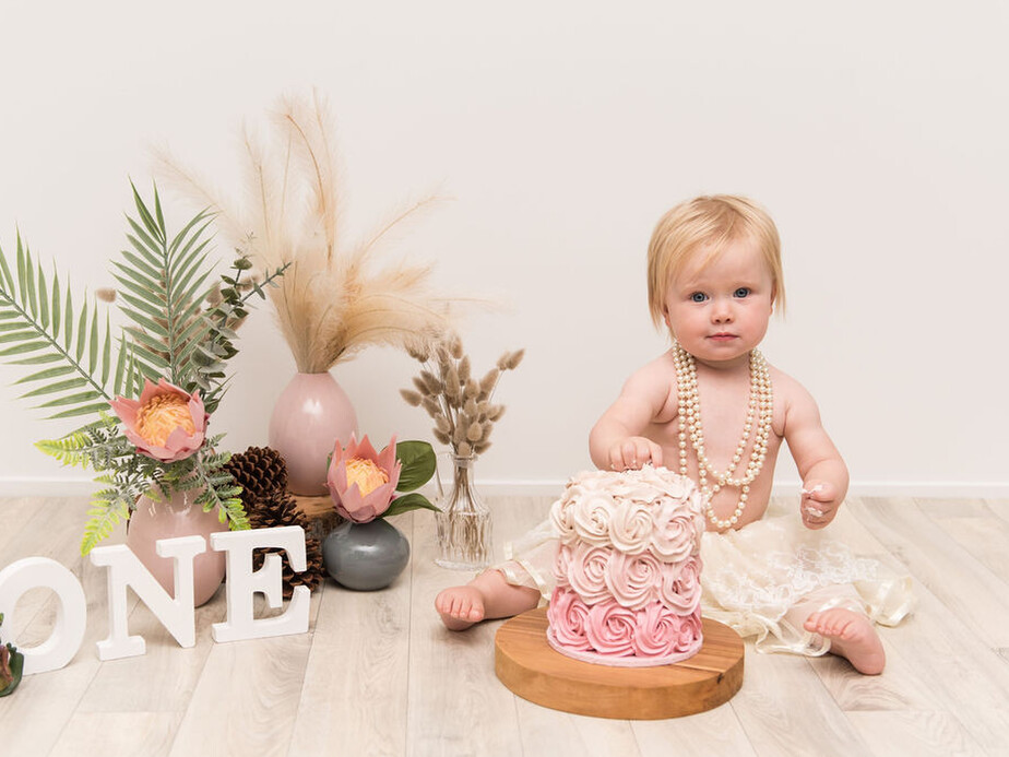 Tauranga Photographer.  Jackie O'Photography.  Cakesmash Photographer Tauranga.  Girl with pink cake and flowers for 1st birthday photoshoot.