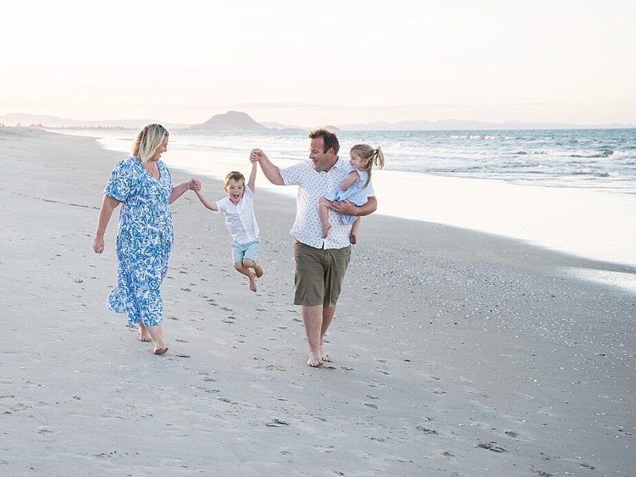 Family on the beach swinging children having fun during family photoshoot in Papamoa