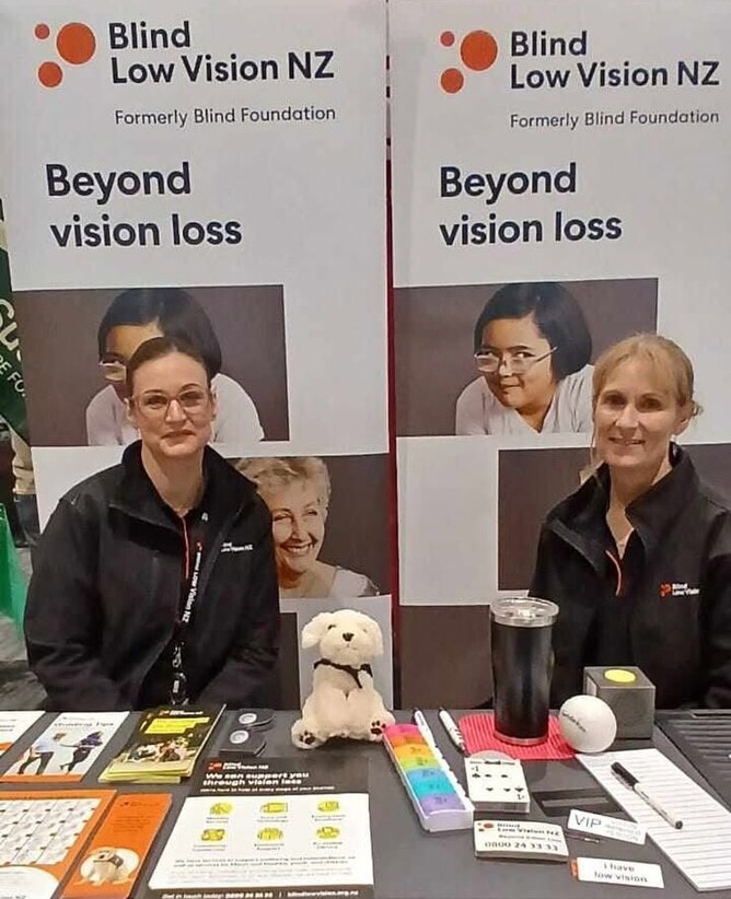 Veronica Rivett, Community Volunteer Coordinator and Erin Leonard, Sport and Leisure Advisor for Blind Low Vision NZ, are smiling while seated behind a table.