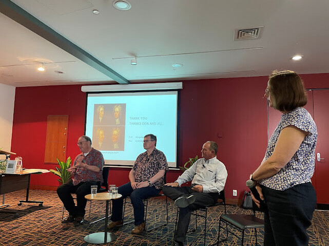 Three men seated and a woman standing.