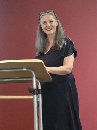 Tania Mace, at a lectern, smiles at the camera.