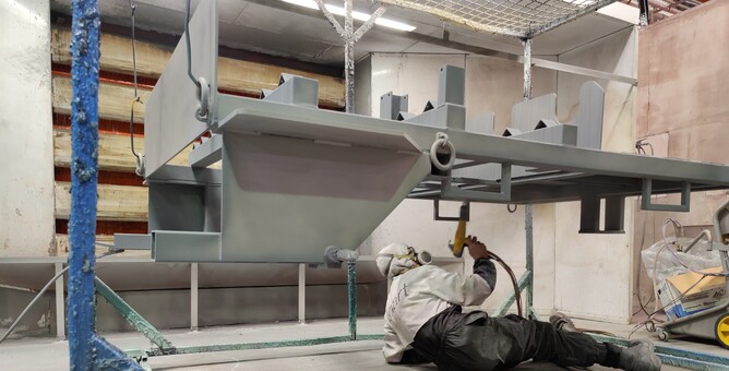 Photo of man inside Hamilton Industrial Powdercoating workshop zinc priming a large item