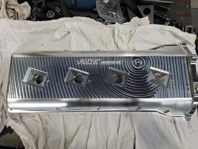 Machined aluminium part with concentric toolpath patterns and two rectangular openings, engraved with “RUSE” logo.