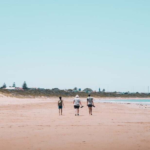 Three people walking down a beach together.