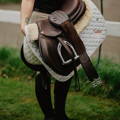 equestrian holding a saddle, saddle blanket and horse accessories