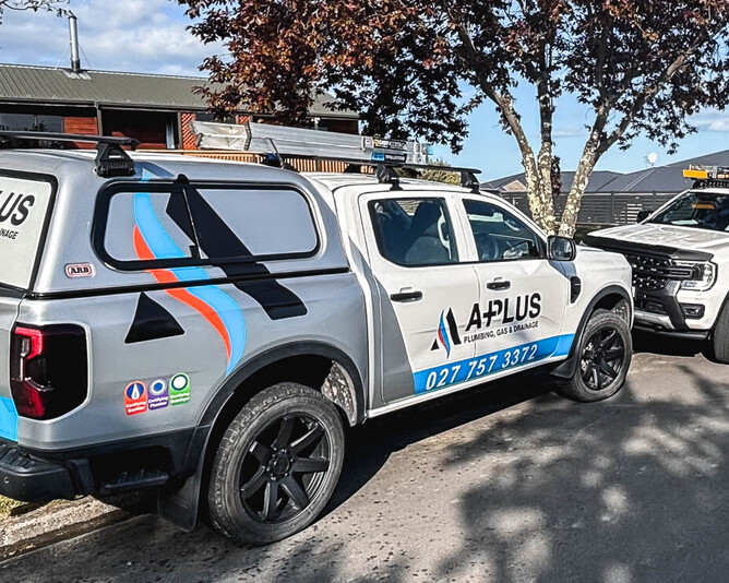 white ford ranger ute parked on the side of teh road underneath a tree with a plus plumbing and gas branding signwritten on it.