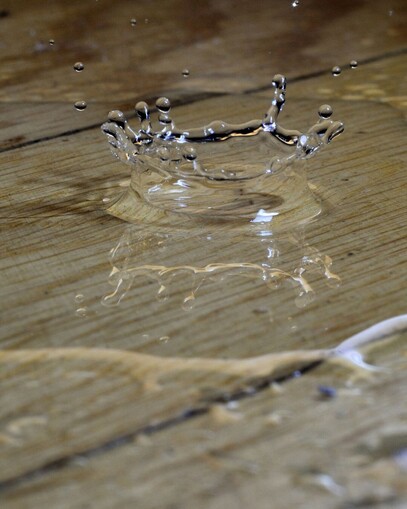 water drop splashing into a puddle on a wooden floor