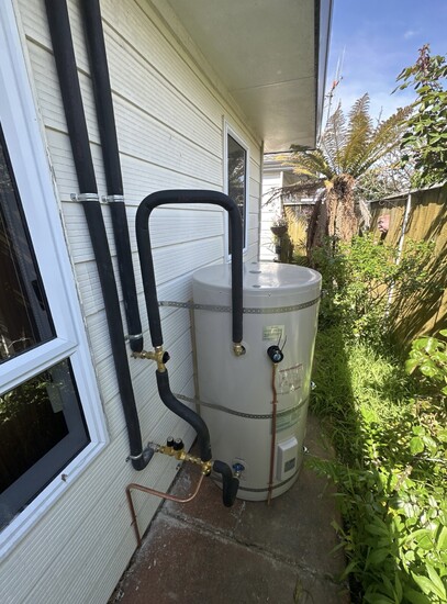 outdoor electric hot water cylinder sitting on the concrete path beside a white weatherboard house