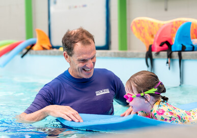 Swimming instructor teaching pre-schooler to kick