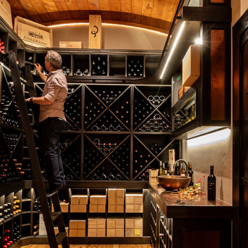 man climbing a ladder and looking at wines in the wine cellar. 