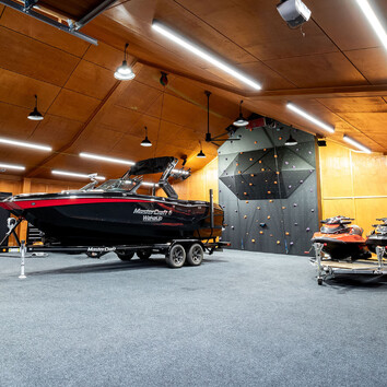 Modern fishing boat on a trailer in a large timber garage. Black climbing wall on the far side.