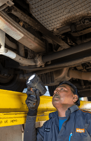 man looking under heavy truck with a flash light inspecting truck for certificate of fitness (cof)