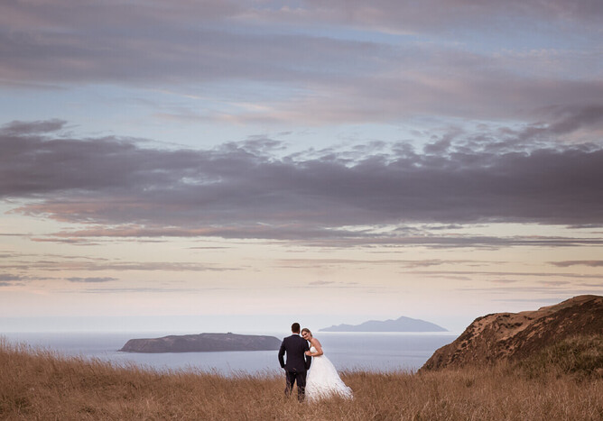 photograph of bride and groom on thier wedding day at boomriock at sunset with mana and kapiti islands