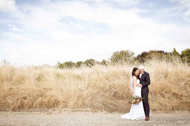 photograph of bride and groom with a blue sky and long summer grass behind them used for a blog on plaiining a post covid wedding my mel waite photography