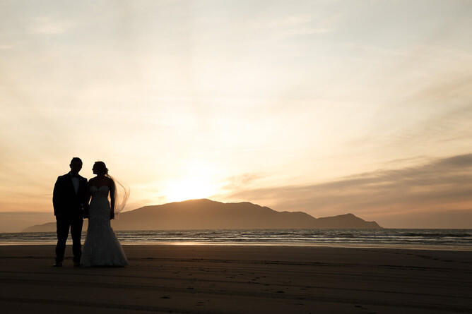 photo of bride and groom on thier wedding day on kapiti beach looking at kapiti island at sunset