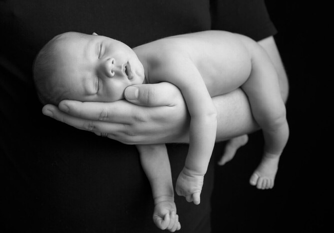 Black and while photograph of a newborn baby girl asleep on her fathers arm in the Mel Waite photography Studio