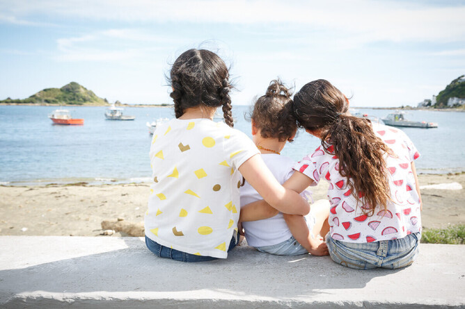three sister sitting on the break wall in island bay wellington during a family photography session