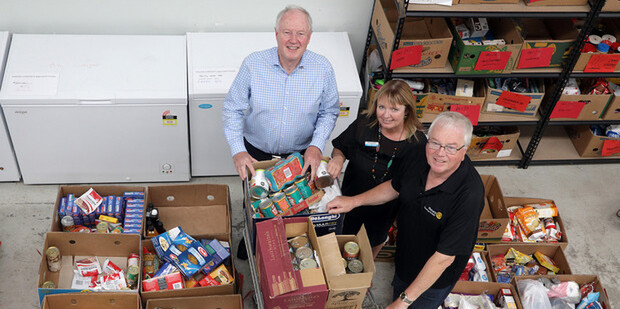 Three Tauranga Foodbank team members stand with food parcels