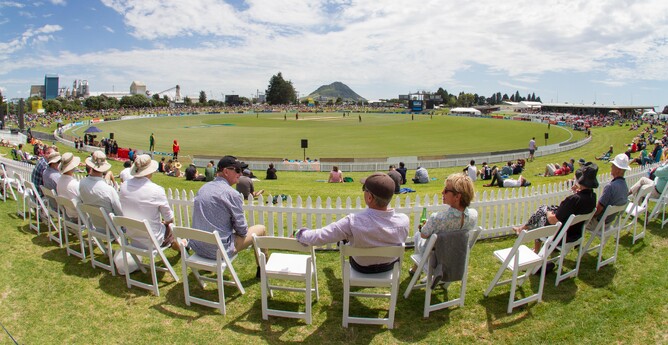Spectators sit in white chairs around Bay Oval watching game