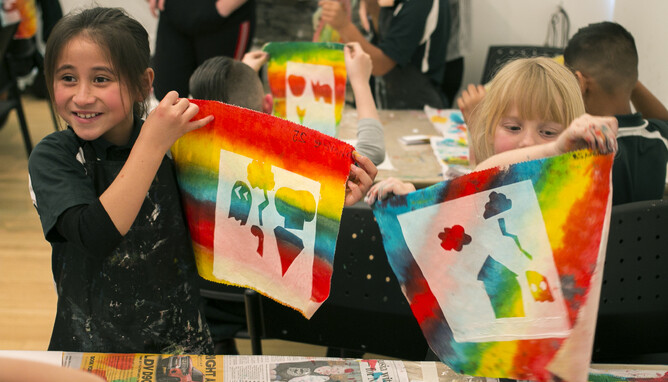 Two girls hold up colourful painting they have created