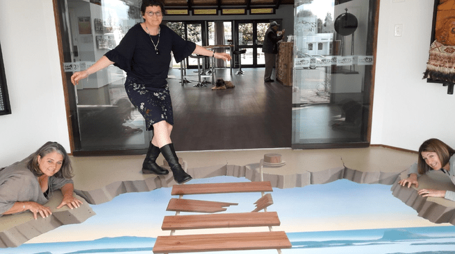 Three Katch Katikati team members pose with stepladder mural on floor