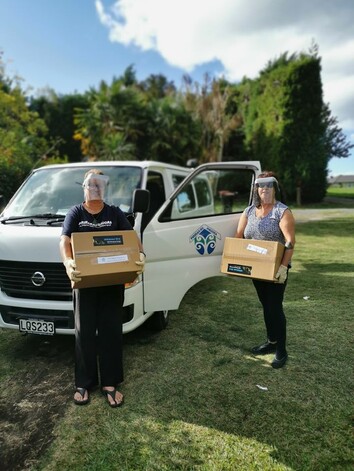 Two Pirirakau Hauora team members carry care packages from van