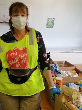 Salvation Army volunteer wearing mask stands by food parcels