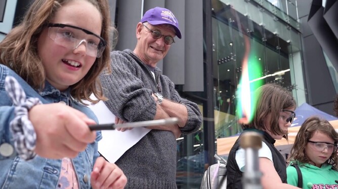 Girl wearing goggles creates green flame on bunsen burner