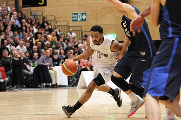 Basketball player dribbles ball around two opposing players