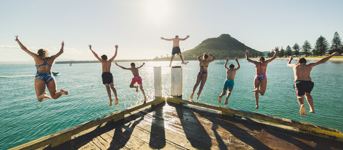 Eight young people jump into water in front of Mount Maunganui
