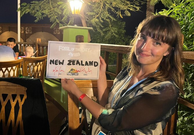 A woman holds the 'Fossil of the day award' certificate at COP27 while smiling sheepishly