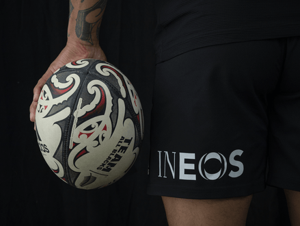 An image of a rugby ball being held next to some shorts with the INEOS logo