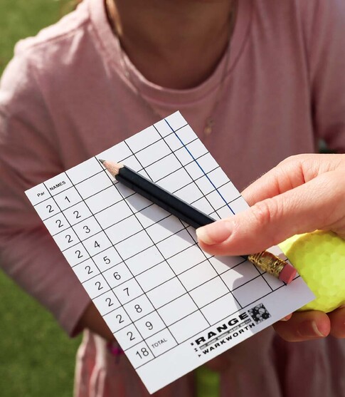 Holding a mini golf scoring card with pencil and golf ball in hand