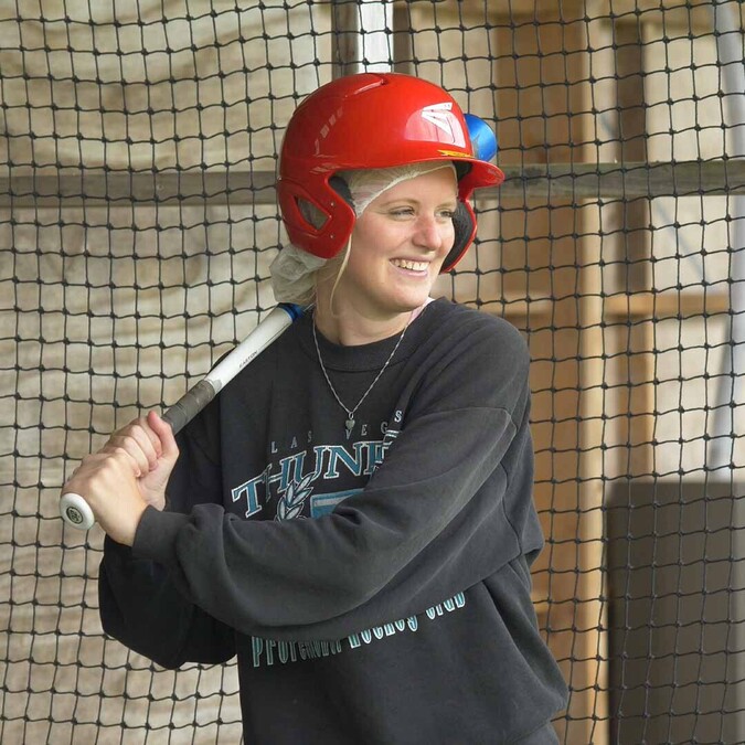 Close up of woman in batting cage about to swing bat, wearing red helmet
