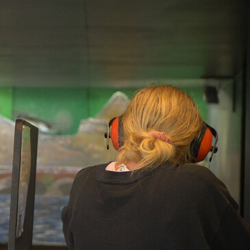 Woman facing toward indoor shooting range and aiming air rifle