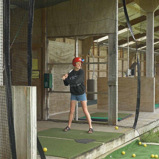 Woman standing in baseball batting cage with red helmet