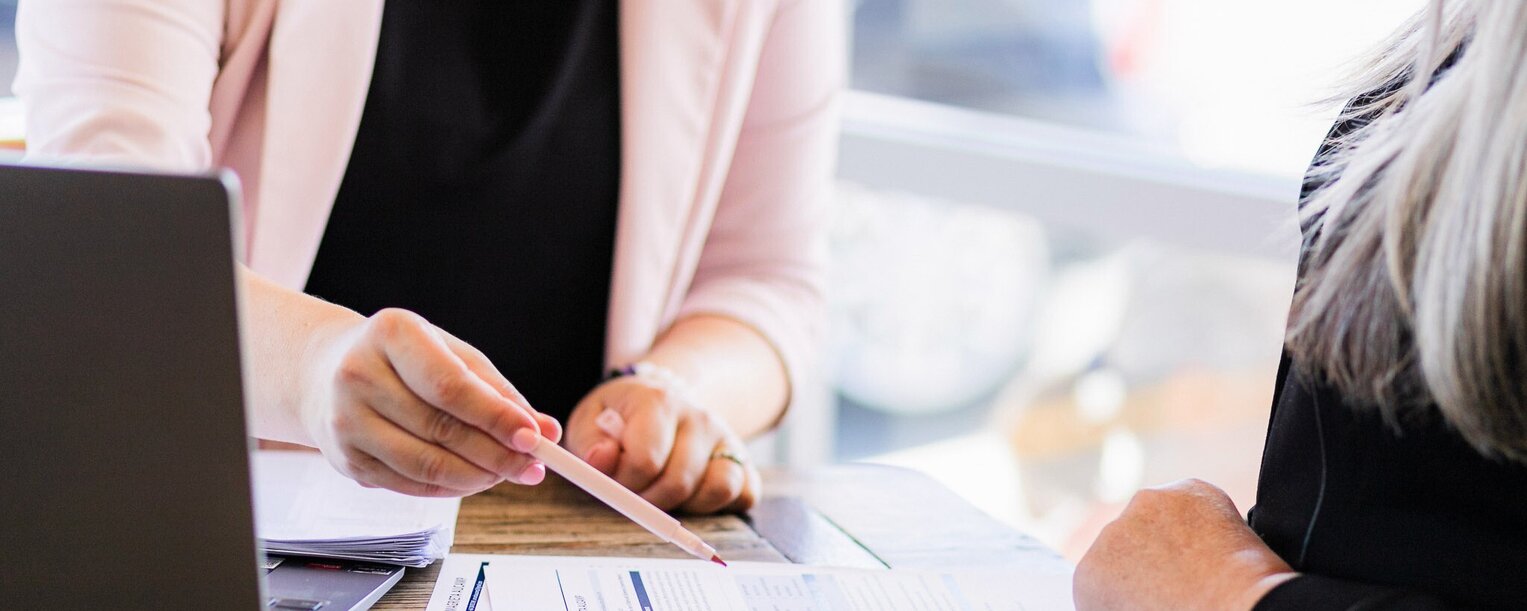 A CV writing consultant reviews a client’s resume at a wooden table, highlighting key points with a pen during a one-on-one career consultation.