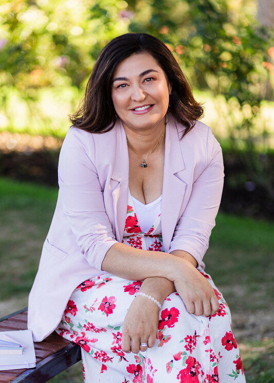 Sarah Wrightson, founder of CVs by Sarah, sitting outdoors in a floral dress and light pink blazer, smiling warmly at the camera.