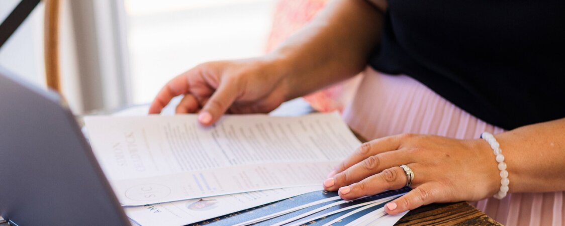 Close-up of Sarah reviewing a stack of printed CVs at a wooden desk with a laptop and smartphone, representing CV writing services by CVs by Sarah.