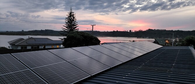 Solar panels installed on residential rooftop in Pukehina, sunset over water in background