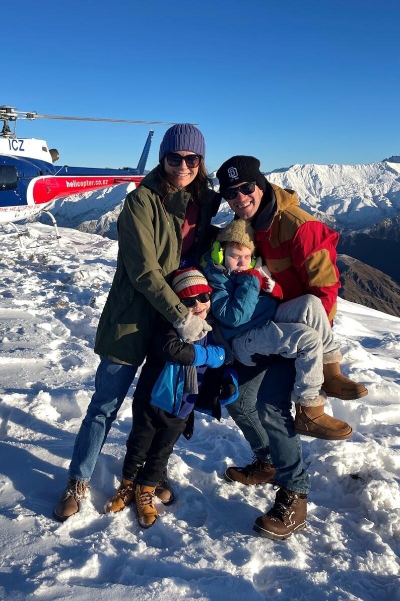 Family on a snowy mountain in New Zealand with a helicopter in the background, father holding his son