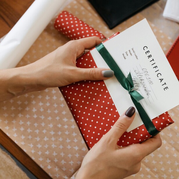 Picture of a ladys hands holding a gift wrapped box which has a gift voucher attached