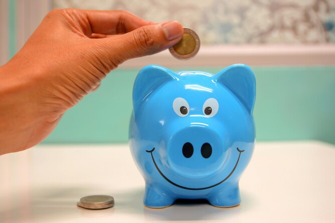 Hand placing a coin into a piggy bank, symbolising saving money and cultivating a positive money mindset